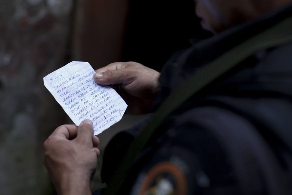 Офицер BOPE читает записки — предположительно, от наркоторговцев, — в которых перечисляются суммы, выплаченные людям, сообщавшим преступникам о присутствии полиции.